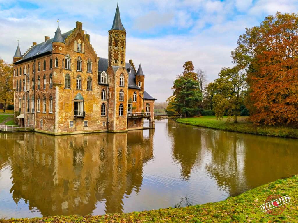 Wissekerke Castle in Bazel, Belgium, surrounded by a calm moat and surrounded by trees with autumn-colored leaves.
