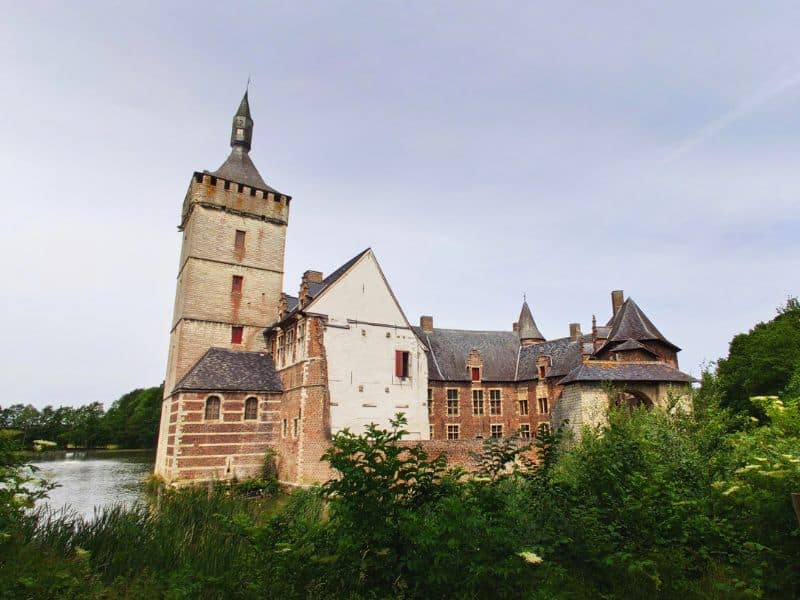 Kasteel van Horst in Belgium, featuring a charming medieval castle surrounded by a picturesque moat and lush greenery. The castle's stone walls, towers, and arched bridges create a fairytale-like atmosphere against a serene landscape.