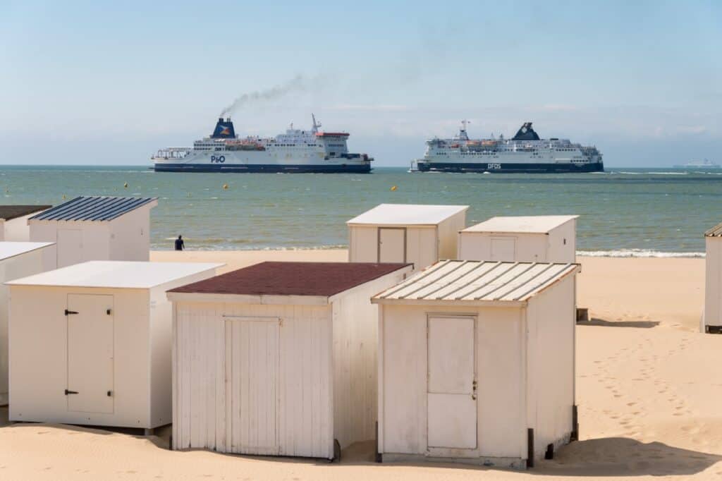 Beach view with beach huts and two ferries in the distance.