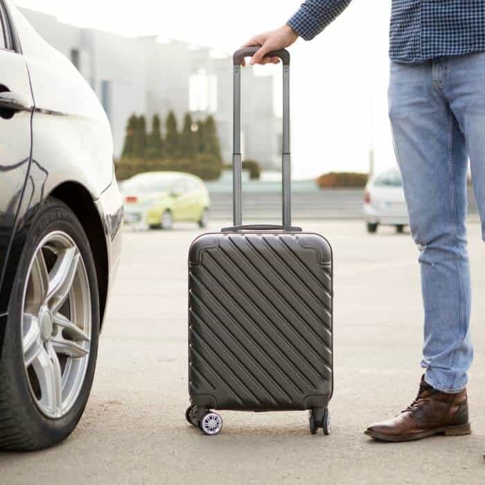 A cropped photo of a man with a suitcase heading towards his rented car.