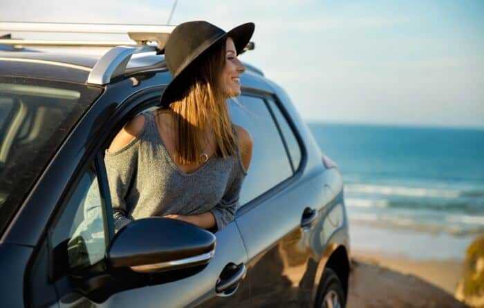A woman with a hat gazing at the beach in her rented car.