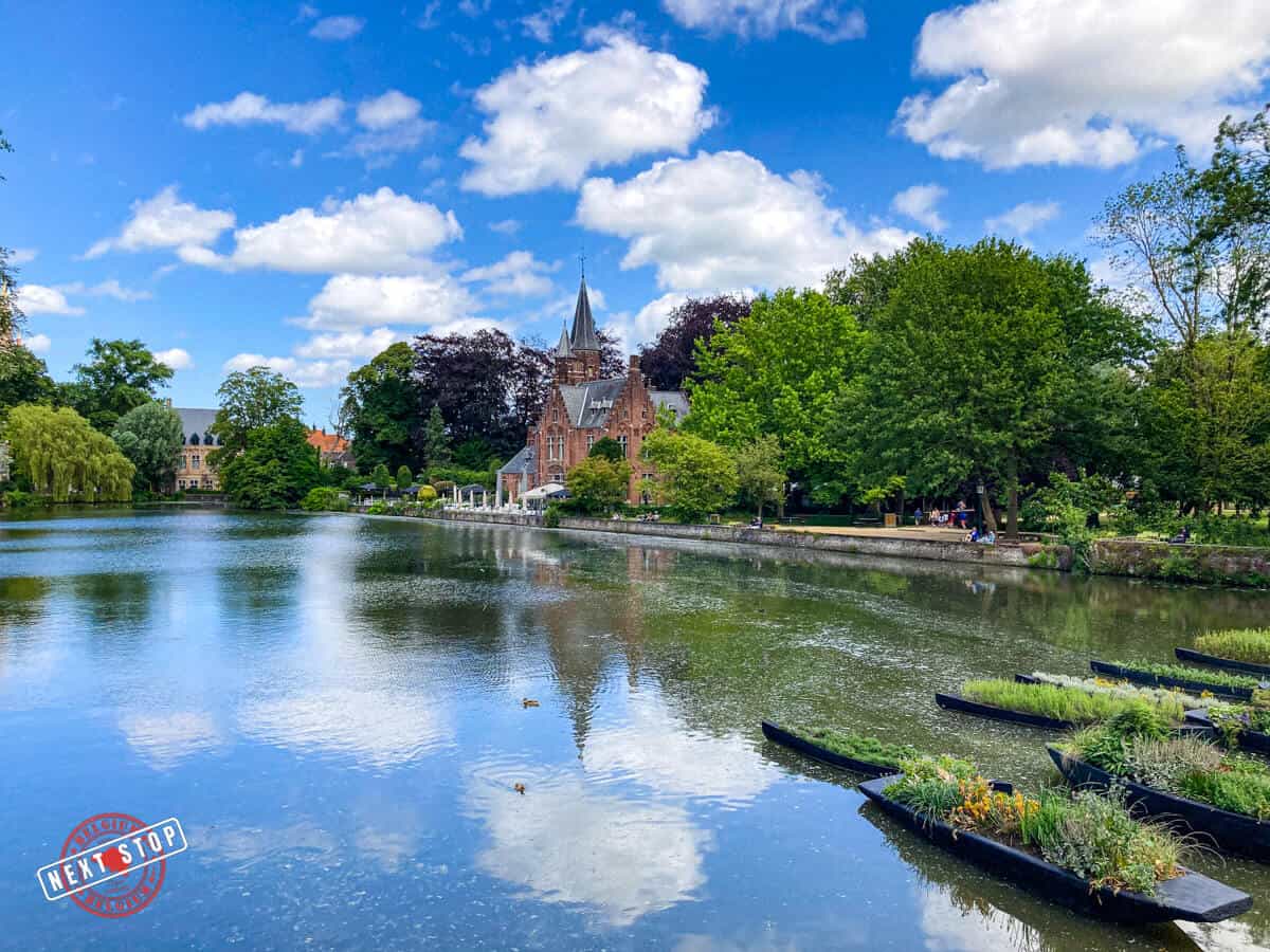 A peaceful view of the Minnewater Lake surrounded by lush greenery, the Minnewater Castle and other medieval architecture.