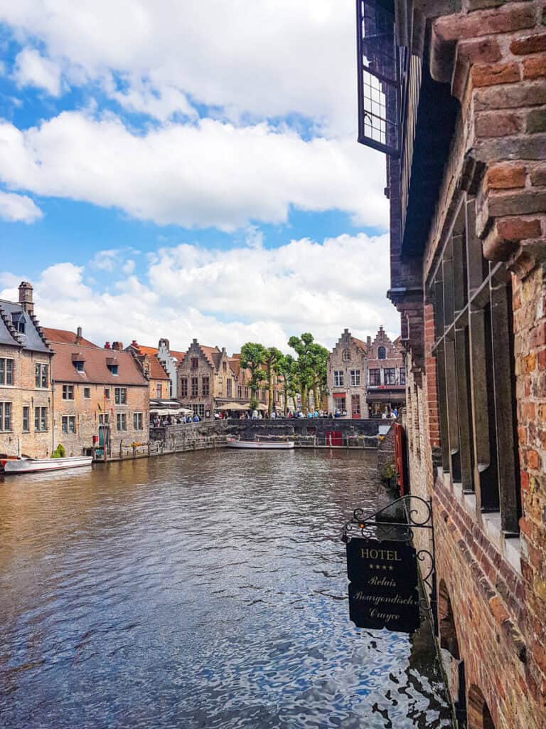 Scenic canal view from Rosary Quay in Bruges, Belgium, showcasing charming medieval buildings with red-tiled roofs reflected in the calm water.