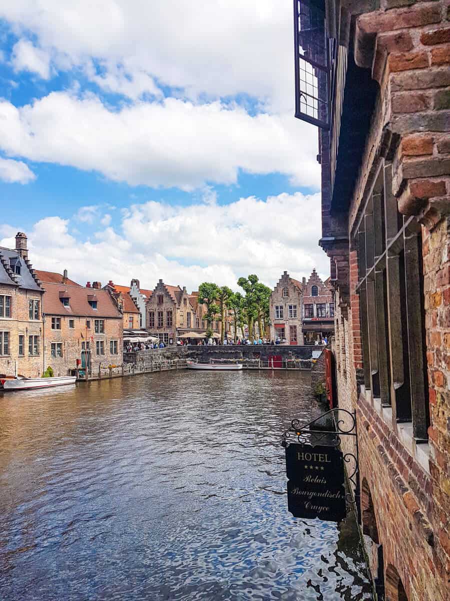 Scenic canal view from Rosary Quay in Bruges, Belgium, showcasing charming medieval buildings with red-tiled roofs reflected in the calm water.