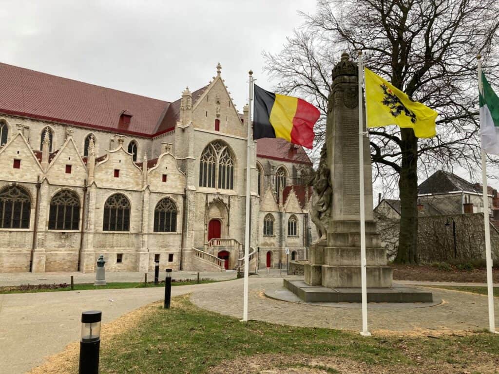 Square with statue and 2 flags, the belgian one and the Flanders one, in front of the St Hermes church in Ronse.