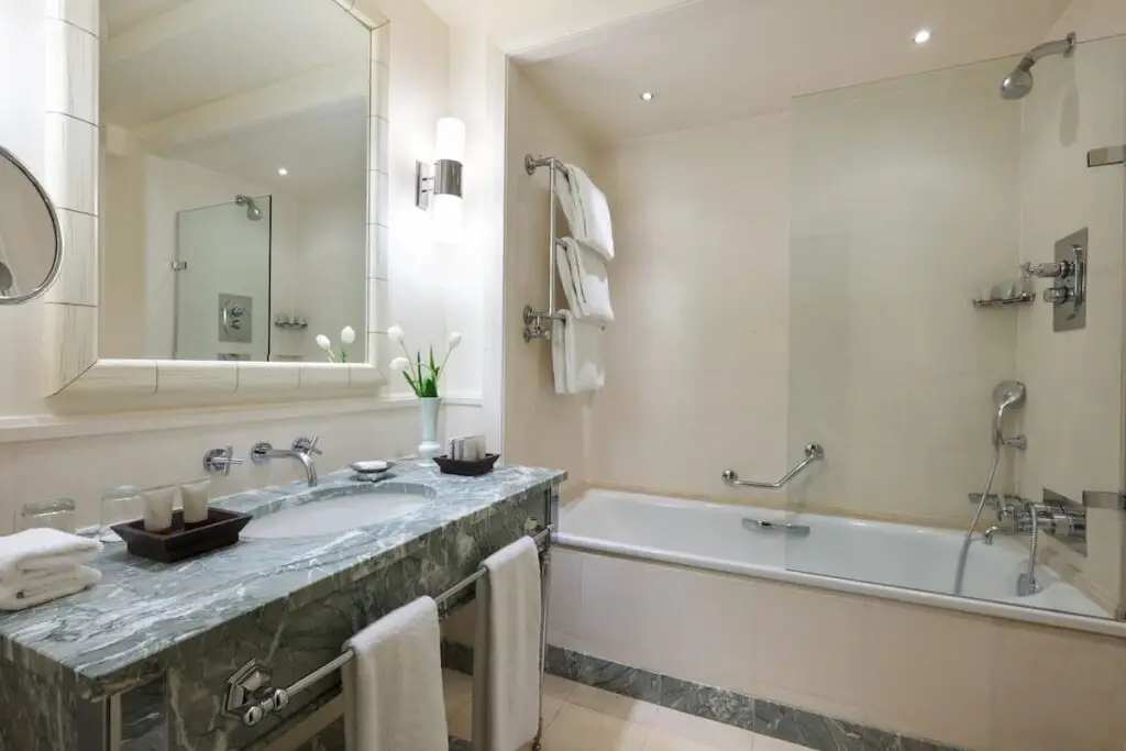 A hotel bathroom with bathtub, shower, mirror, and sink on a marble counter