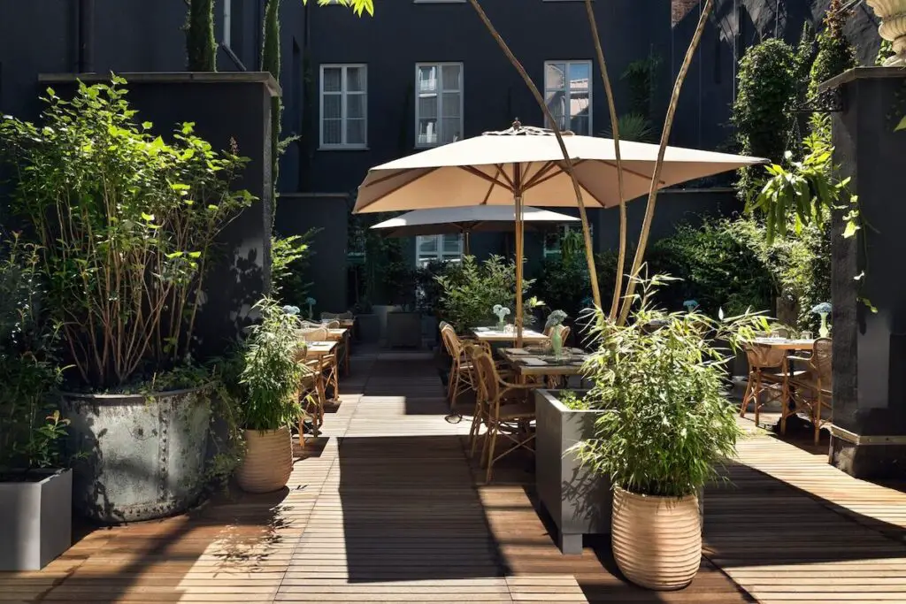 An outdoor area of a hotel with tables, chairs, umbrella shad, and plants