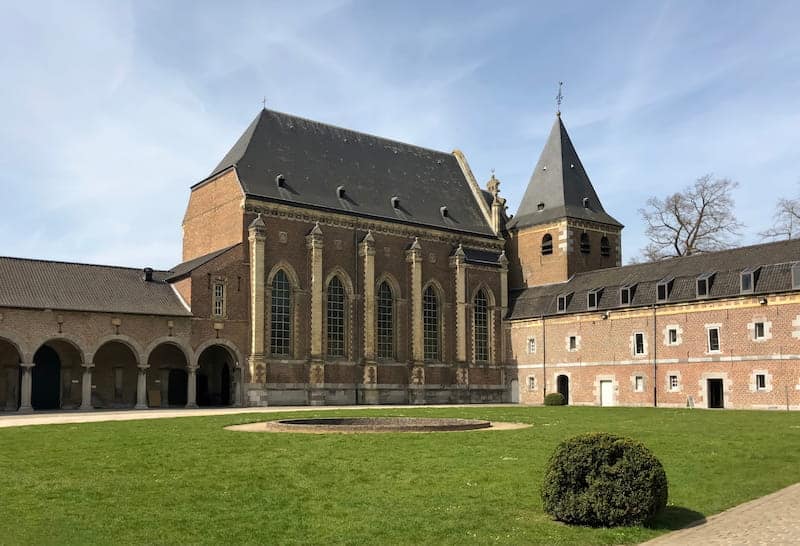 Alden Biesen Castle in Belgium, showcasing its impressive, sprawling complex with elegant stone architecture and intricate detailing. The castle is surrounded by lush gardens and serene grounds.