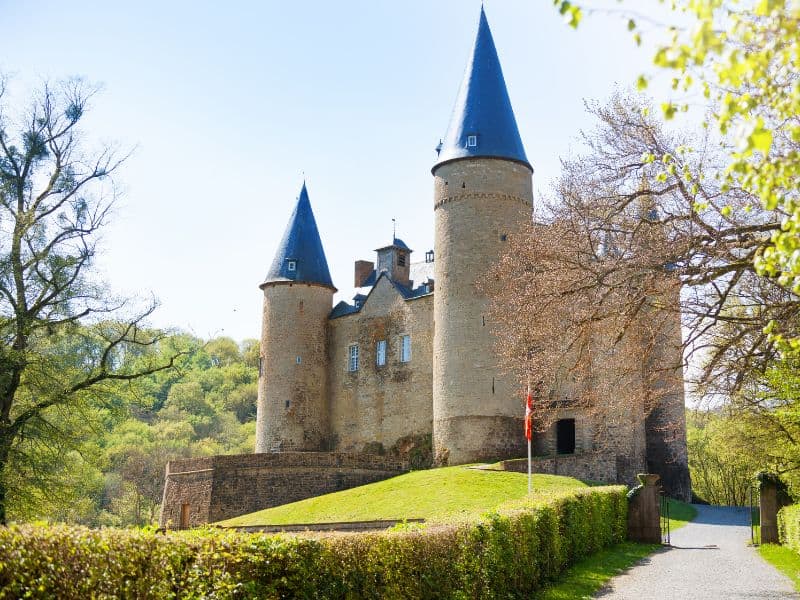 Historic Vêves Castle in Belgium, featuring a dramatic medieval architecture with tall spires and a picturesque setting surrounded by lush green trees.