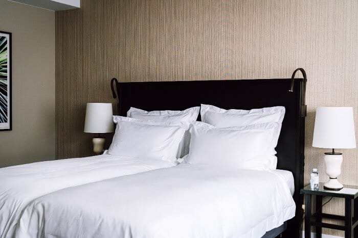 A bedroom in one of the best Brussels hotels with dark bed frame, white bed, and dark bedside tables with white lamps