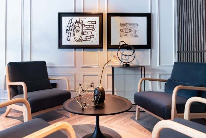 A sitting area in one of the best hotels in Brussels City Centre, with dark circular wooden table, wooden chairs with dark cushions, dark art pieces, and framed art pieces on a wall