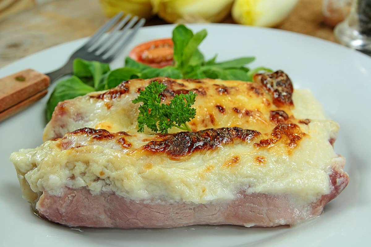 Endive Gratin with Ham on a plate with a sliced tomato, green leafy sides and a fork on it.