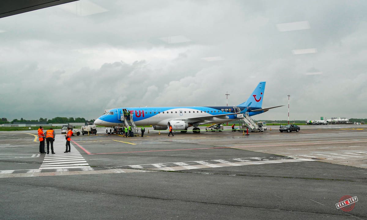 An aiport ramp with a TUI aeroplane and personnel on the grounds preparing to board passengers.