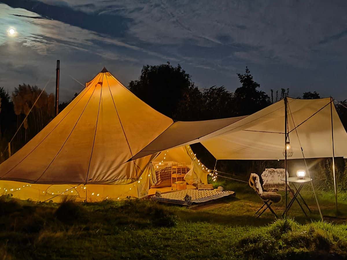 The image depicts the exterior of Au Pied Du Trieu at night, illuminated by warm, inviting lights. The building radiates a cozy ambiance against the night sky, with lights casting a soft glow on its features, creating an inviting and picturesque scene.