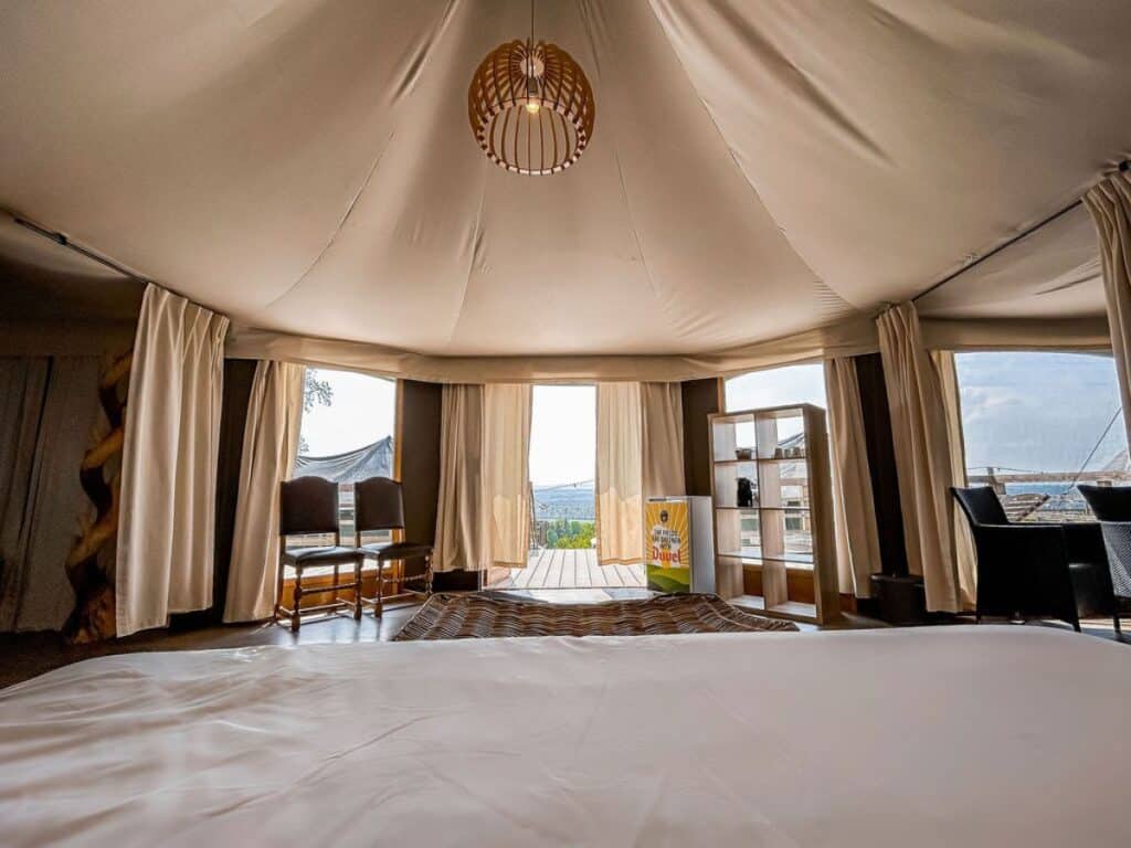 Interior of Green Fields - Durbuy glamping accommodation, featuring large windows offering natural light, a cozy bed and comfortable chairs.