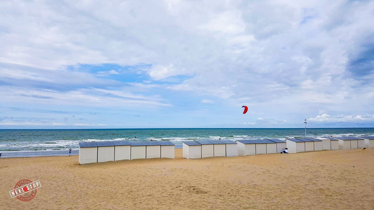 Wide empty beach with a line of beach cabins in front of the sea.