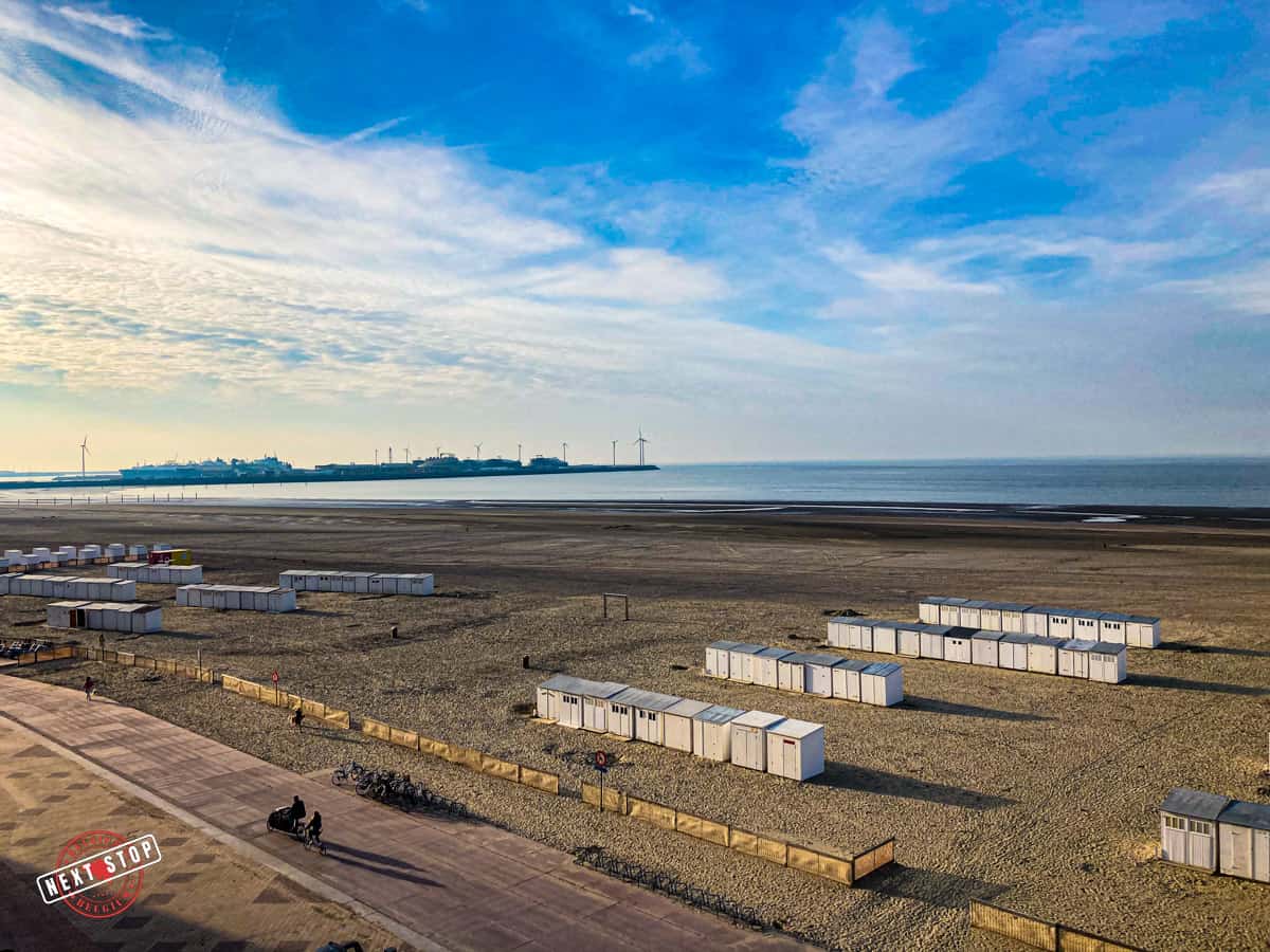 Aerial view of the beach of Knokke Heist with white cabins and the port of Zeebrugge in the distance.