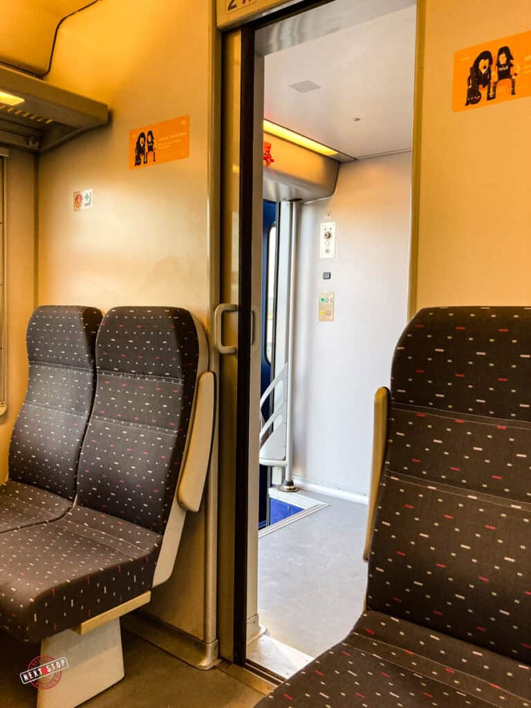 2 seats on one side and 2 on the other, in the middle the door leading to the hallway of a Belgian train.