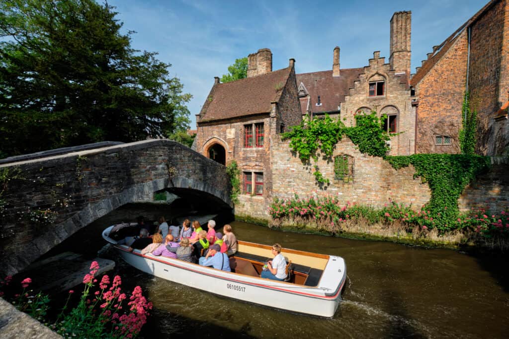 A canal boat tour full of tourist passing under Bonifacius Bridge in Bruges, Belgium.