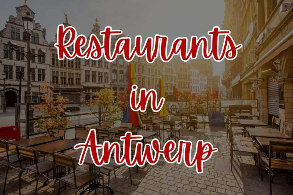 Outdoor café tables and chairs line a cobblestone street in Antwerp during golden hour, with classic Flemish architecture in the background. Bright umbrellas are closed for the evening, and the bold red and white text overlay reads “Restaurants in Antwerp.”