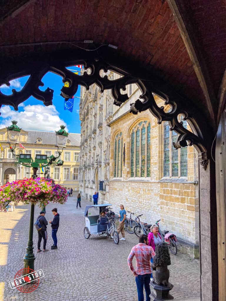 View from Bruges Holy Blood Chapel stairs overlooking Burg Square with a rickshaw, people walking, bicycles, and historic buildings.
