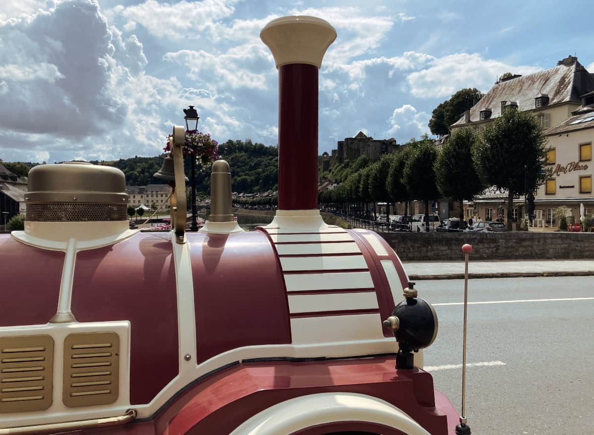 A close-up side view of Le Petit Train in Bouillon, with a scenic backdrop of the Semois River.