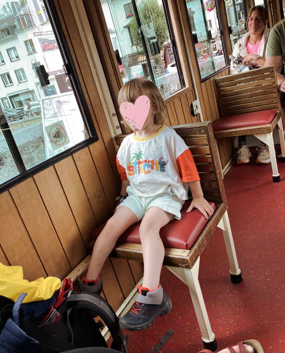 Oscar sits on a wooden bench inside Le Petit Train in Bouillon.