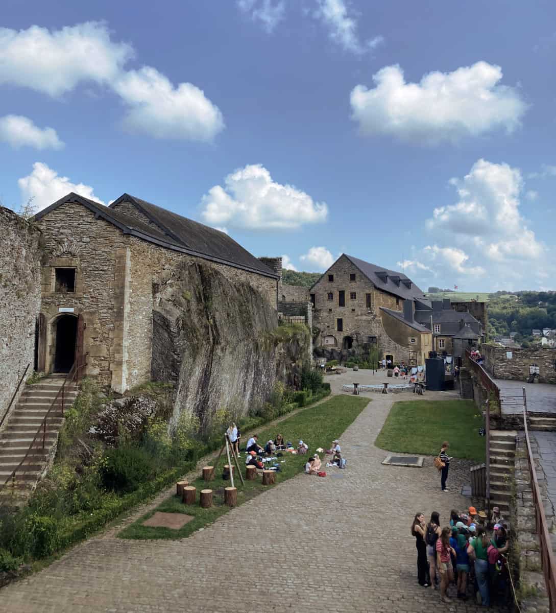 A high-angle view of an inner courtyard at Bouillon Castle in Belgium, filled with tourists on a cloudy day.